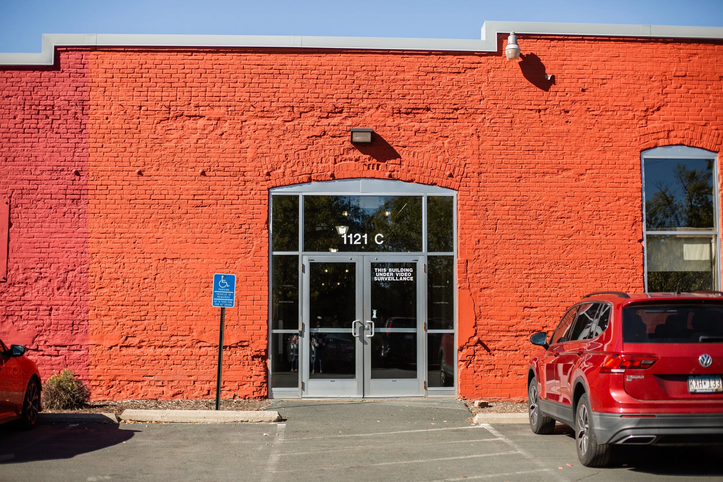 Red brick building with glass doors, a parking lot, and a handicapped parking sign.