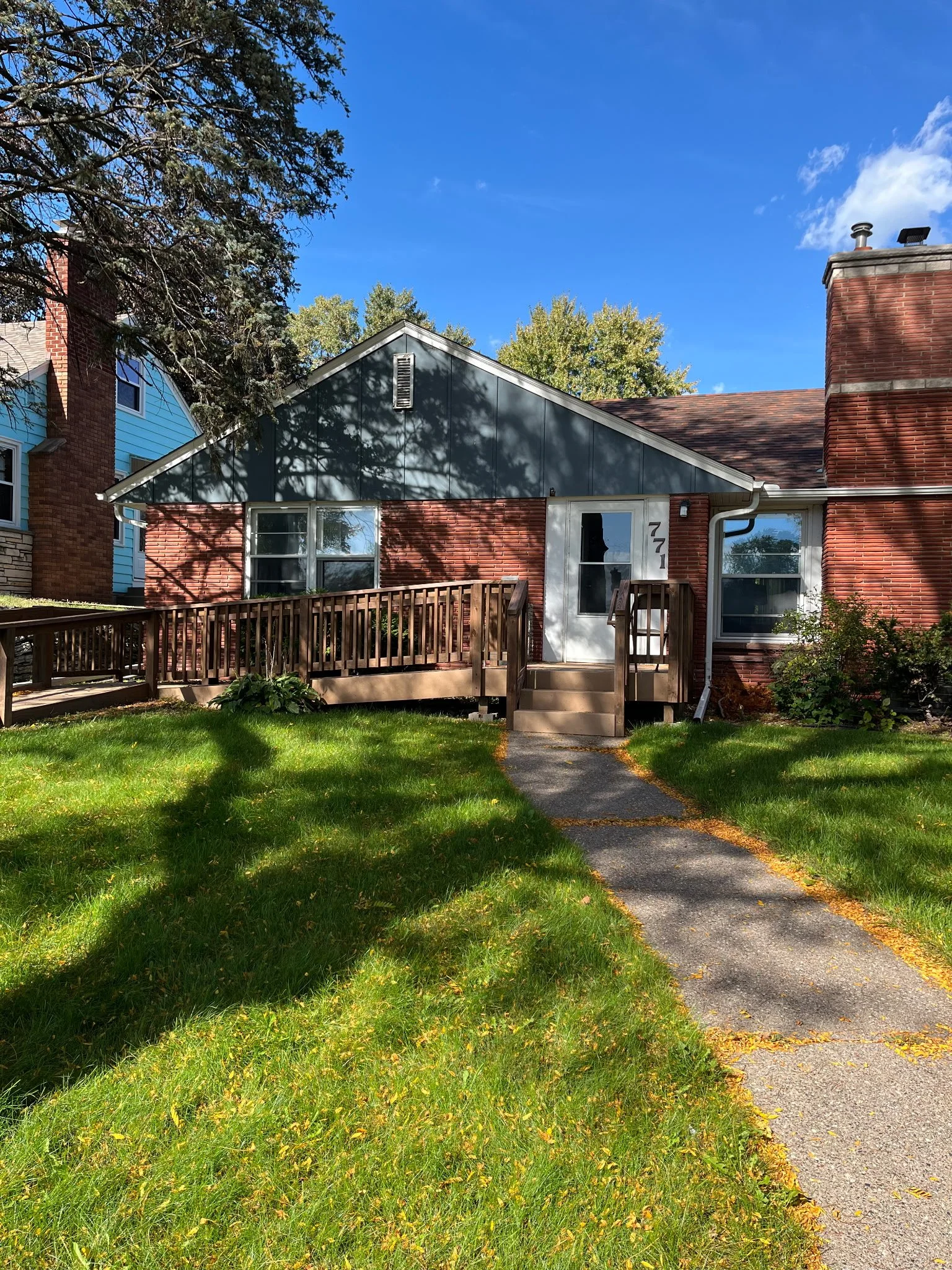Nebraska home: red brick house with blue siding, a front deck with a ramp, and a walkway across a green lawn