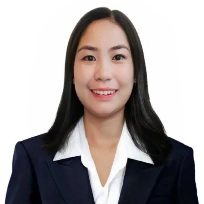 Professional woman with black hair, wearing a navy blazer and white shirt, smiling against a white background.