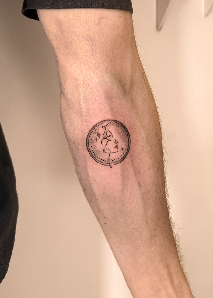 Tatoeage van een abstract gezicht en sterren binnen een cirkel op de onderarm.