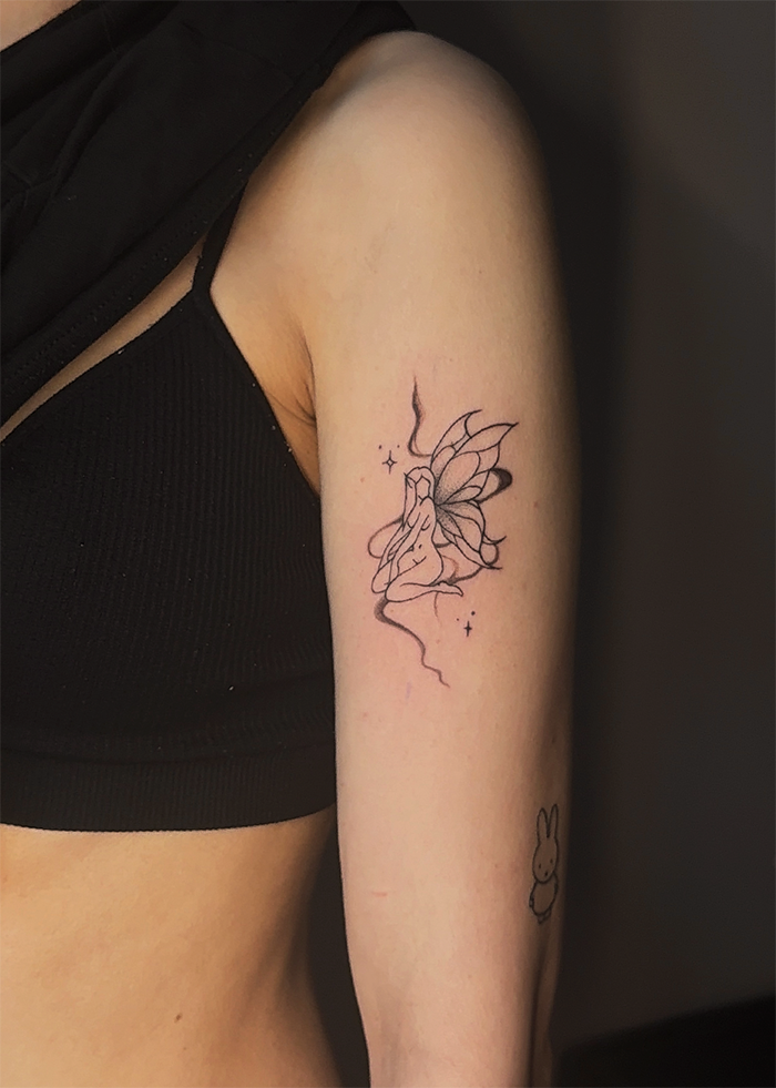 Tatoeage van een vrouwelijke fee met elfachtige vleugels op de bovenarm.