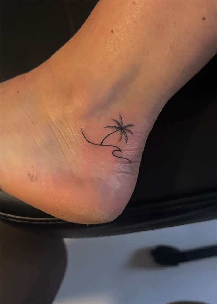 Tatoeage van een palmboom en een golvende lijn onder de enkel op een voet.