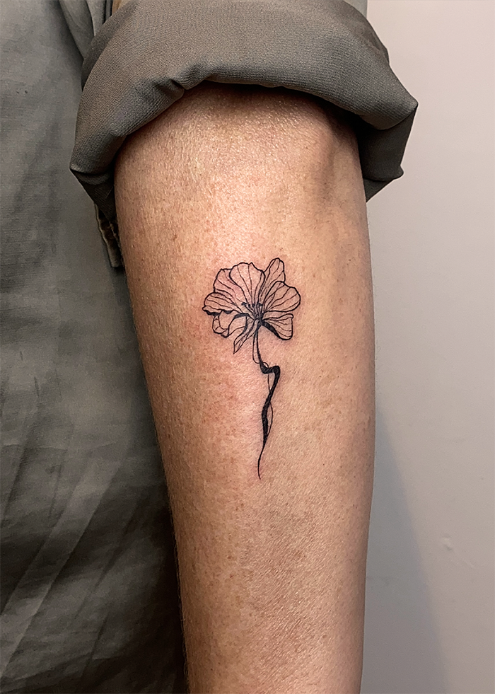 Een tatoeage van een gele bloem met een zwarte steel op de onderarm.