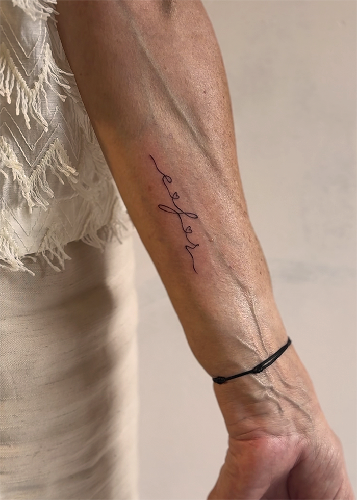 Een close-up van een onderarm met een getatoeëerde naam en een zwarte armband.