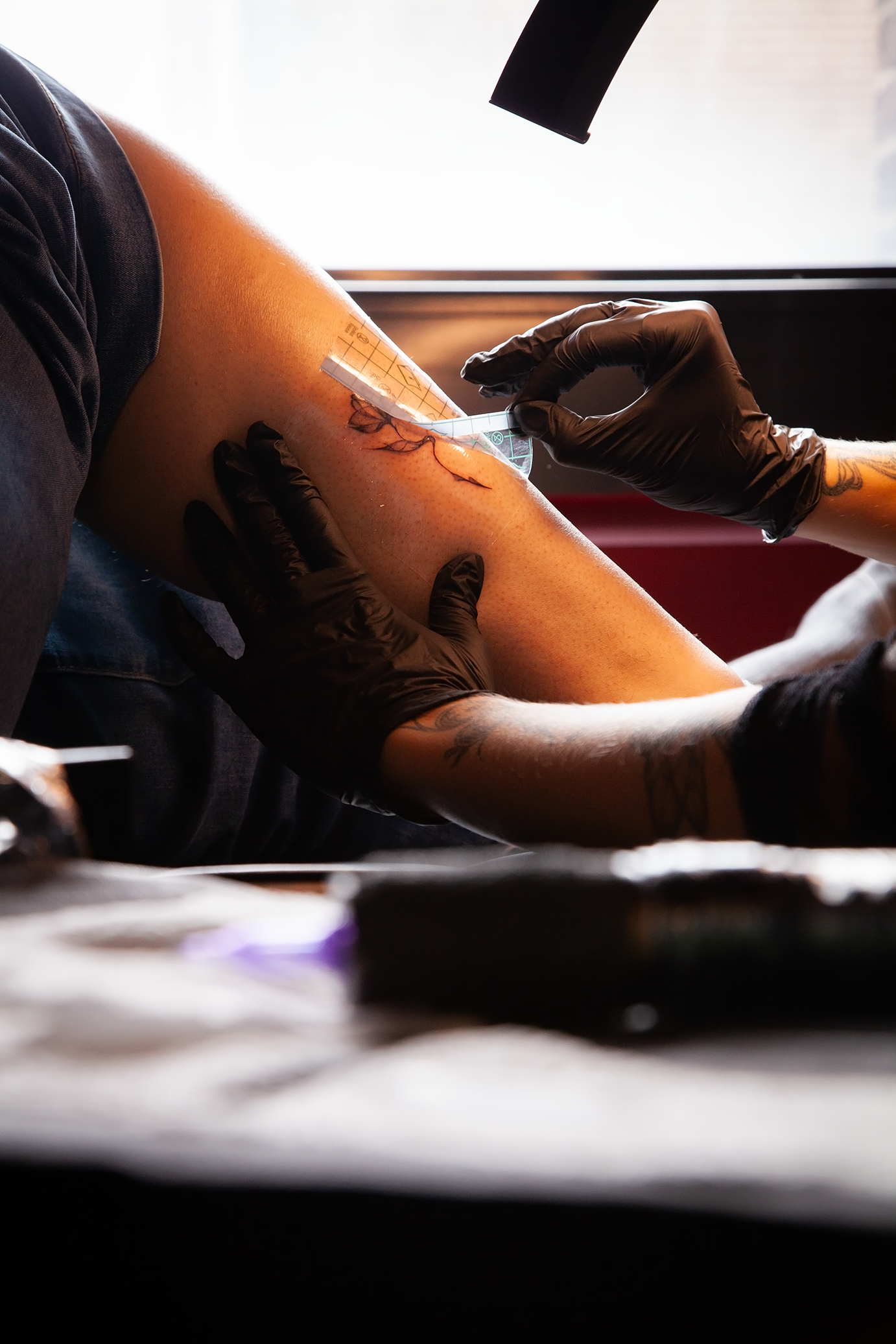 Tattoo artist die een tatoeage zet op de arm van een persoon, met behulp van een meetlint en een meetinstrument in een inktschilderruimte.