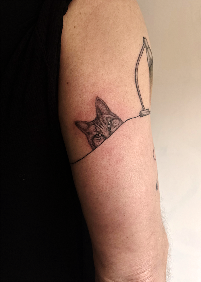 Tatoeage van een kat die uit een lamp kijkt op de bovenarm.