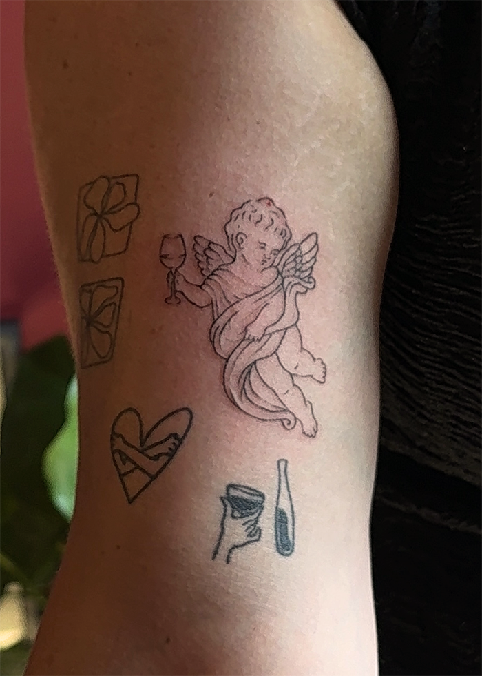Tattoo's op de bovenarm met verschillende tekeningen: bloemen, een engel met een wijnglas, een hart, een hoge hak, en een fles.