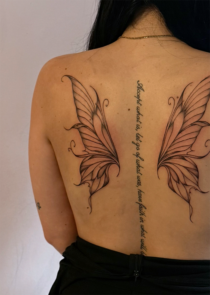 Tatoeage van twee vleugels en een citaat op de rug van een persoon.