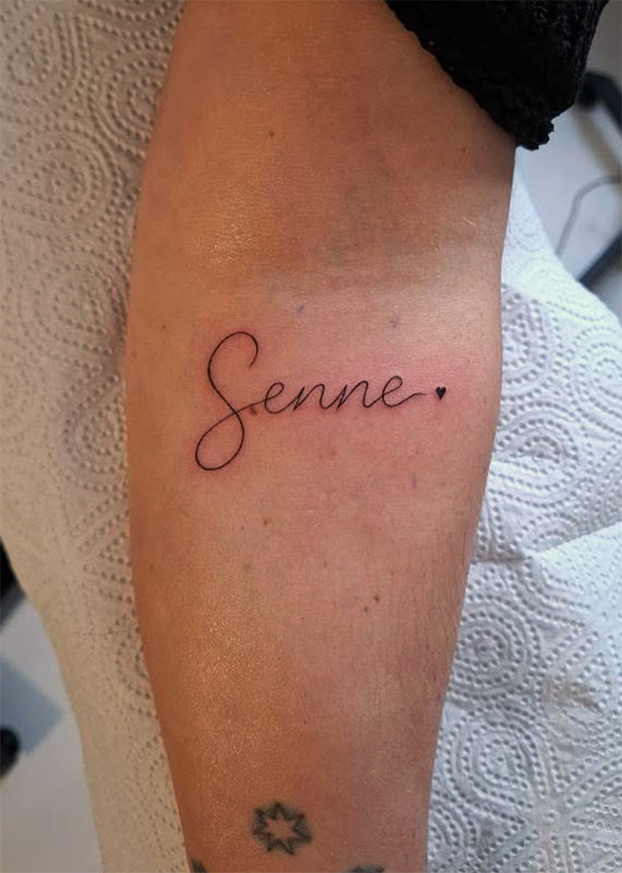 Tatoeage met de naam 'Senne' en een klein hartje op een arm.
