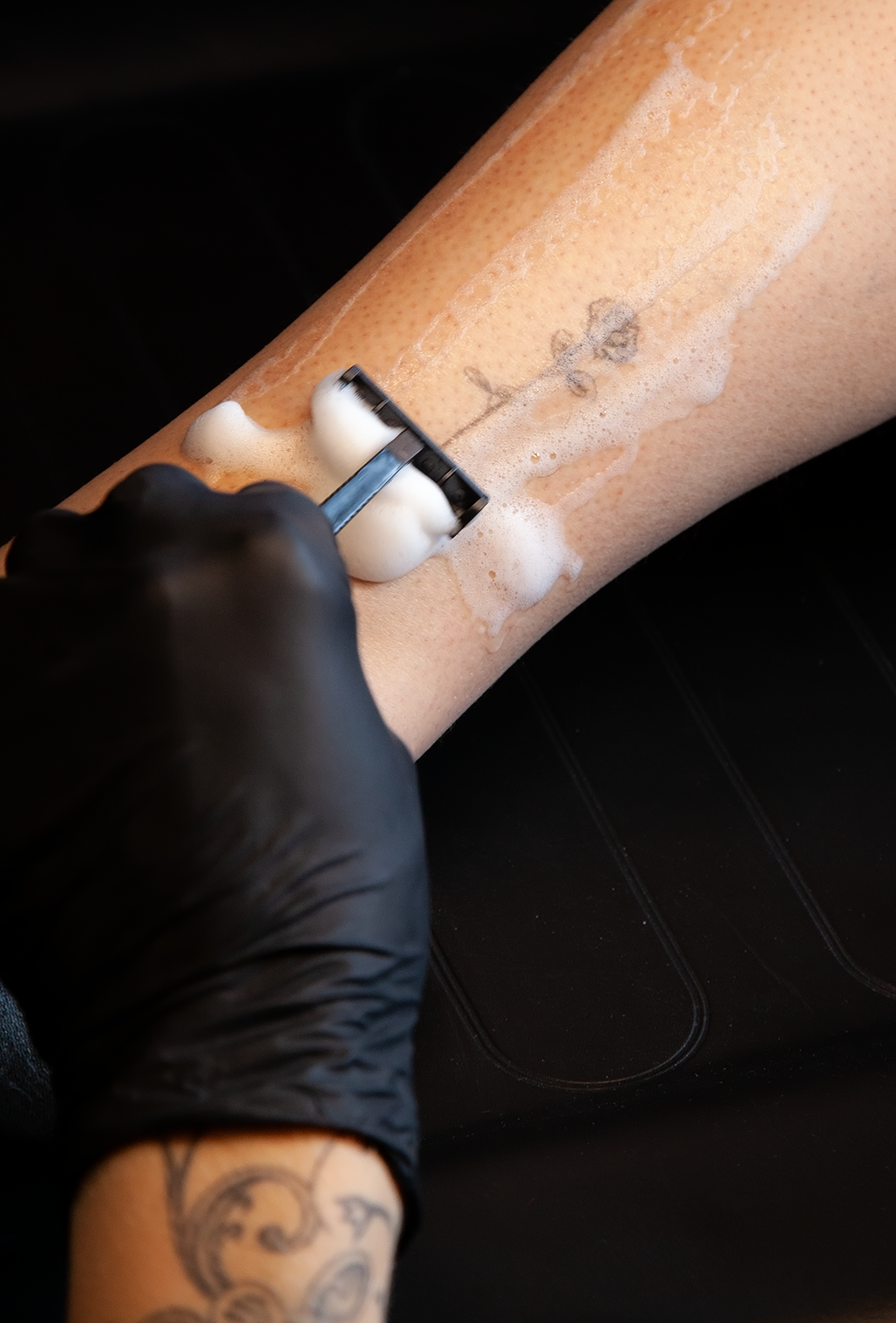Persoon met een tattoo op de onderarm wordt getatoeëerd door een artiest die zeep gebruikt voor de procedure.