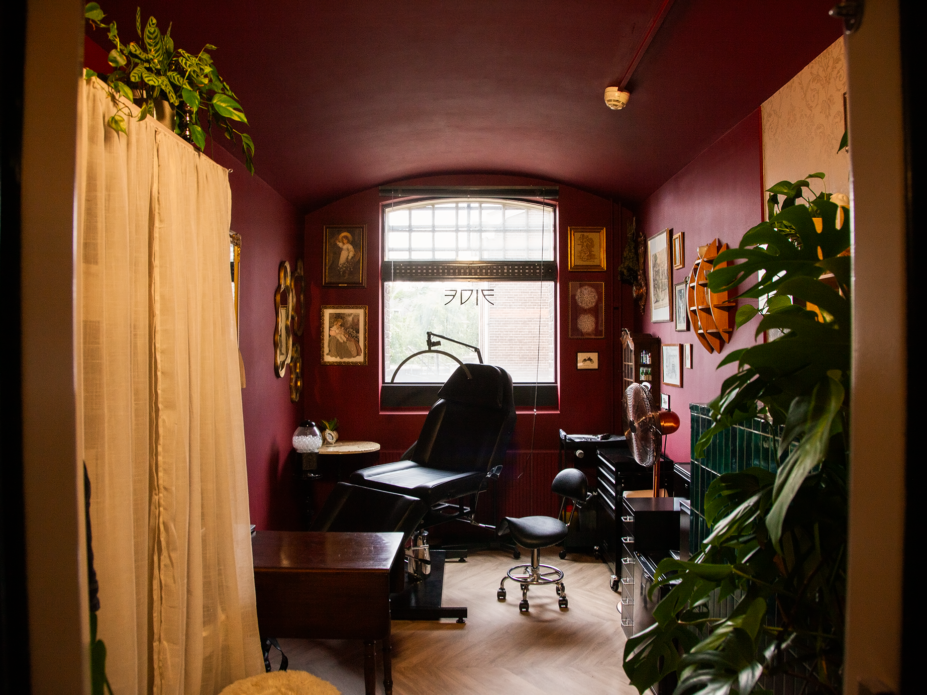 Een gezellige thuiswerkplek met een bureau, bureaustoel en planten, binnenkant van een kamer met dieprode muren en een groot raam.