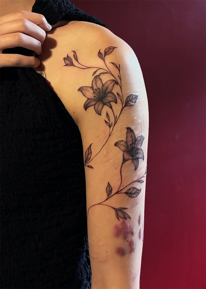 Tattoo van bloemen en bladeren op de bovenarm van een persoon.