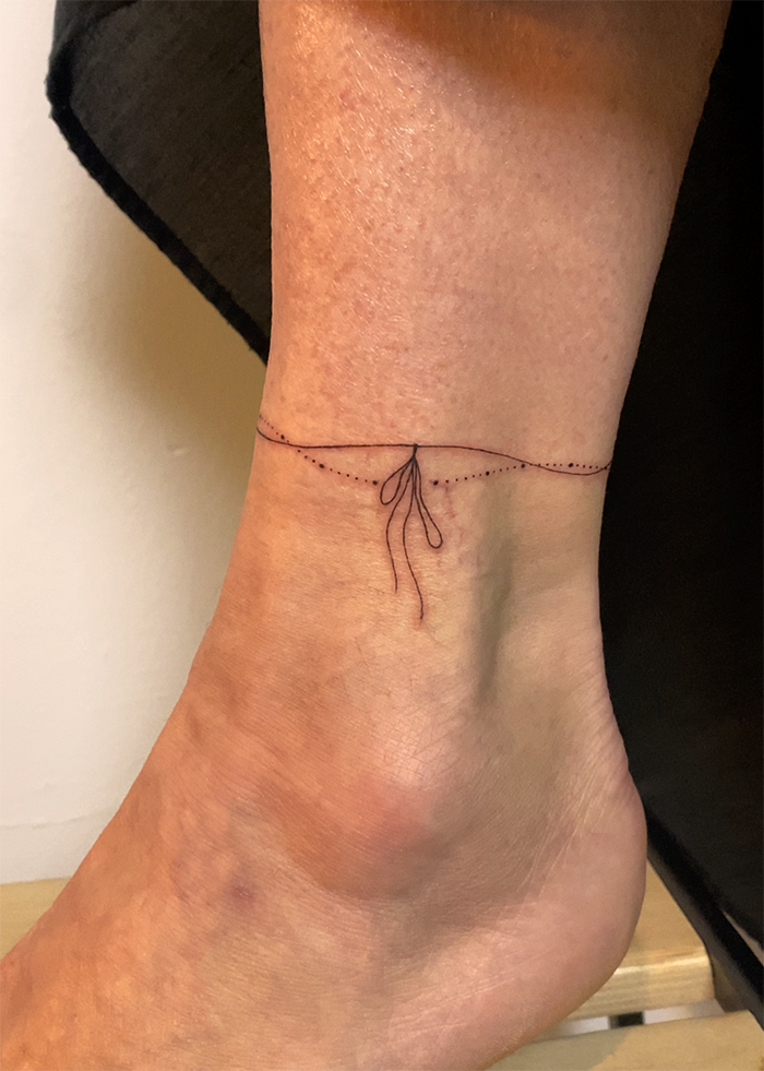 Een enkel met een dunne, minimalistische tatoeage van een touwtje dat een knoop maakt.