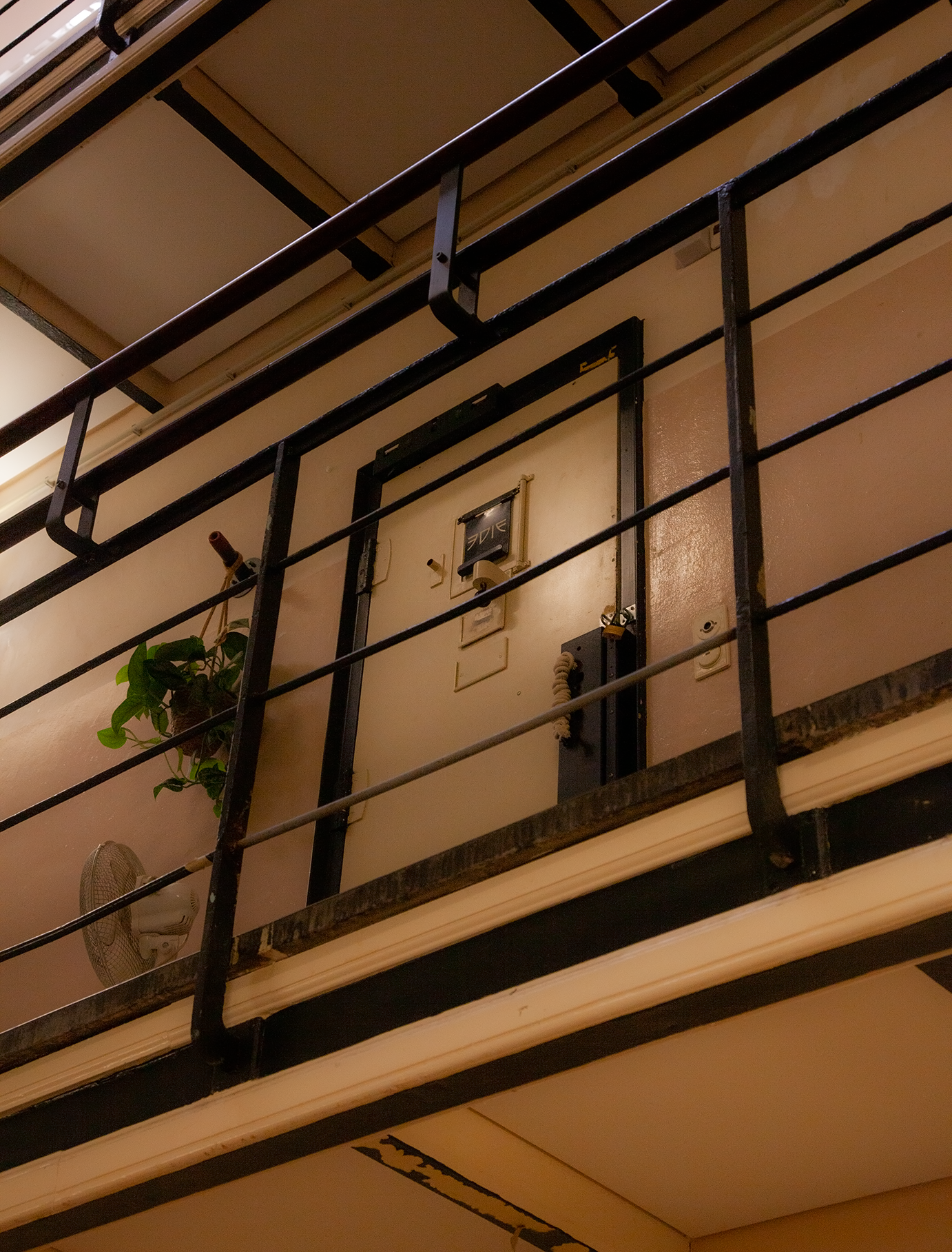 Een binnenverdieping met een balkon, een plantenpot met een plant, een ventilator en verschillende schakelaars op de muur.