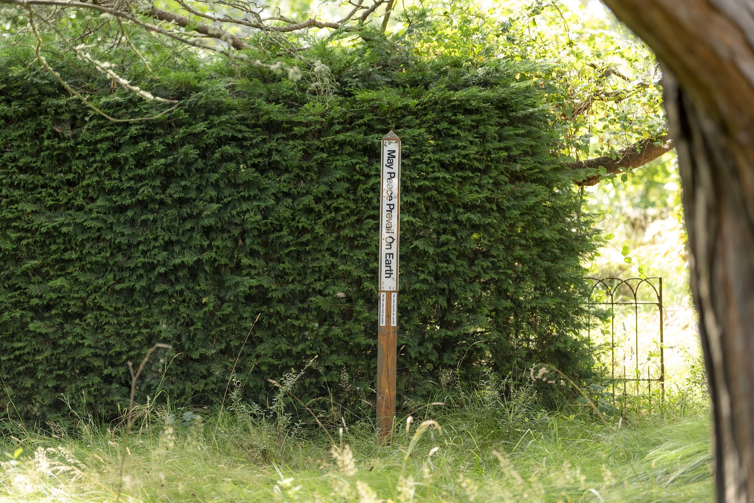 A peace pole standing among trees in the grounds of Cullerne House Findhorn.