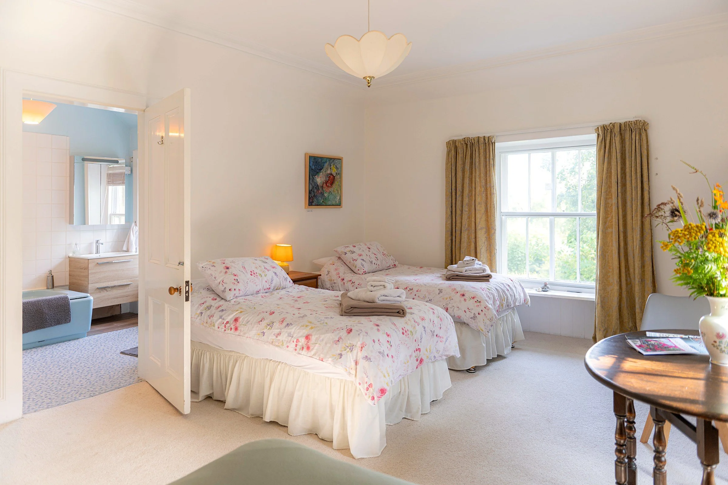 Full view of the Ruby twin room at Cullerne House in Findhorn, showing both beds, the bathroom entrance, garden-facing window and sitting table.