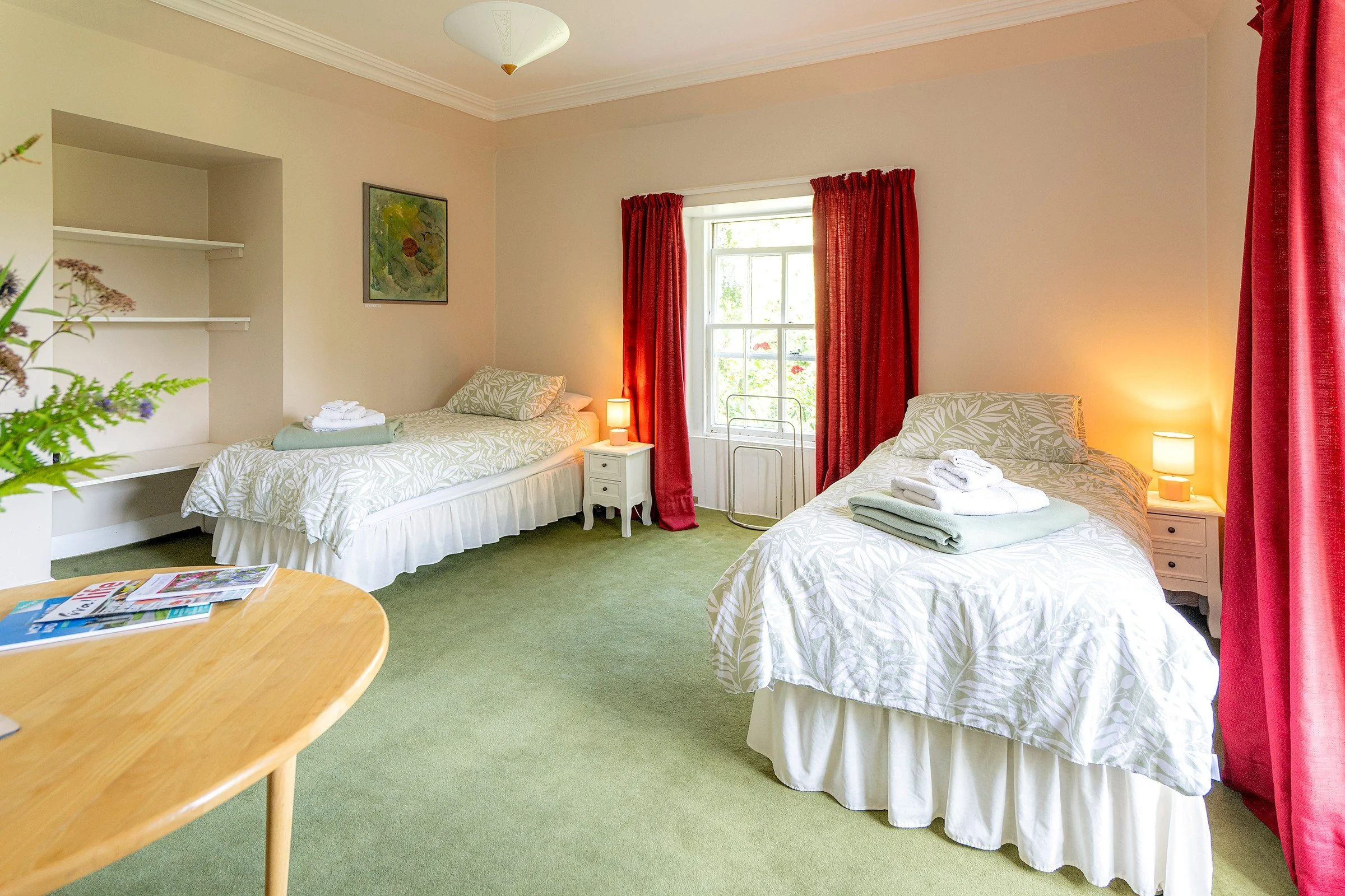 Emerald twin room at Cullerne House in Findhorn with two single beds, red curtains, garden-facing window and sitting table.