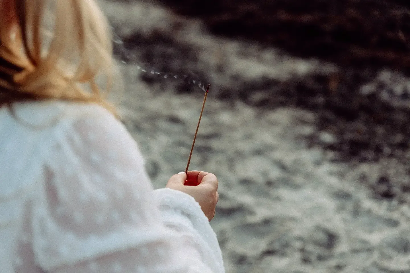 Eine Person mit blonden Haaren hält ein Streichholz vor Wasser, das eventuell ein Fluss oder See ist.