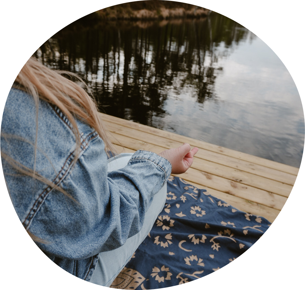 Nahaufnahme einer Person in Jeans sitzt am Wasser auf einem Holzdock, mit einer hand in einer Meditationshaltung.
