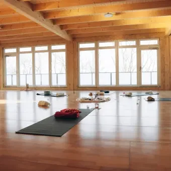Yogamatten und -zubehör in einem hell erleuchteten Holzraum, möglicherweise für eine Yoga- oder Meditationsklasse.