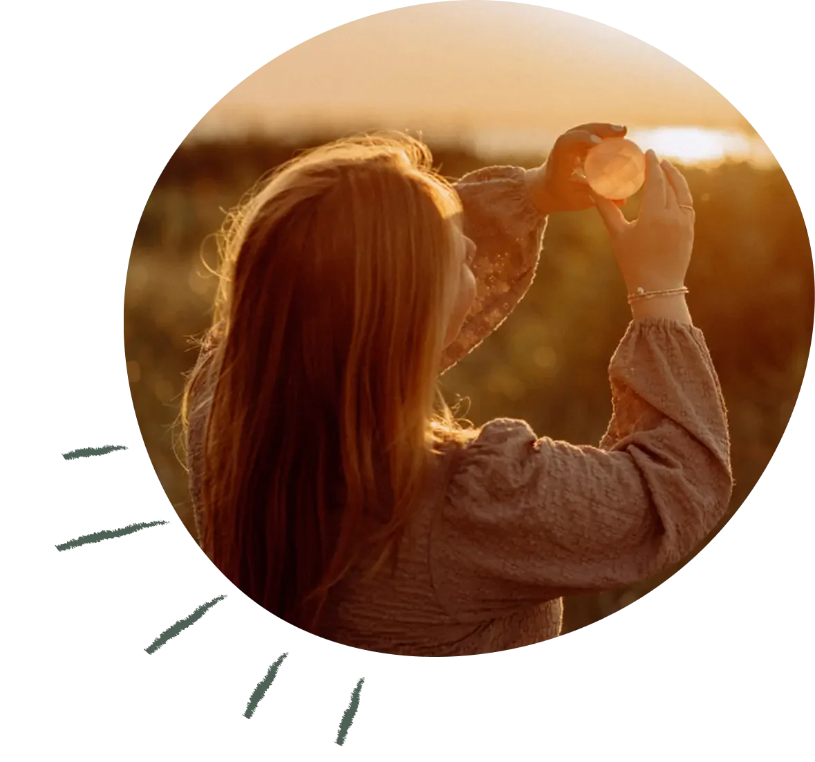 Rothaarige Frau mit lockigem Haar hält eine Glaskugel vor sich in der Abendsonne.
