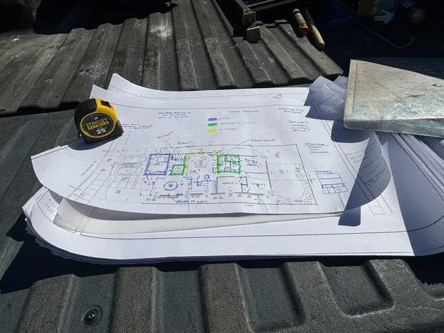 Blueprints and construction tools on a metal surface, including a tape measure and a level.