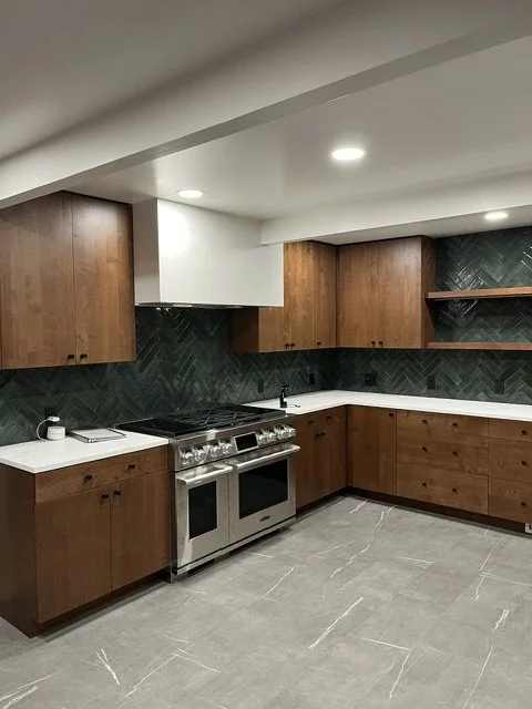Modern kitchen with wooden cabinets, black backsplash, stainless steel oven, and gray tiled floor.