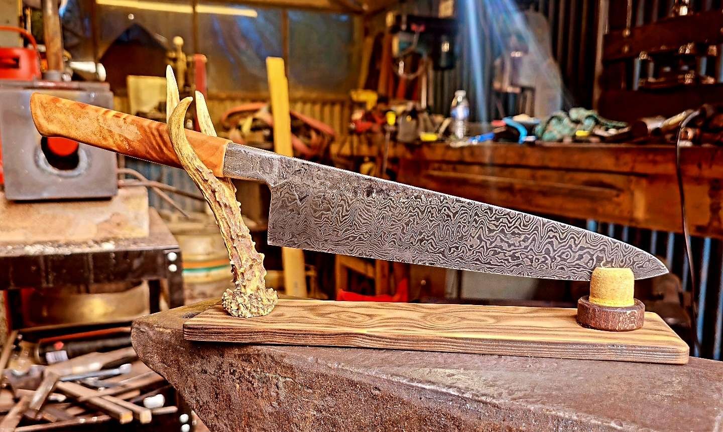 A handcrafted Damascus steel knife with a wooden handle, mounted on a wooden stand in a woodworking workshop.