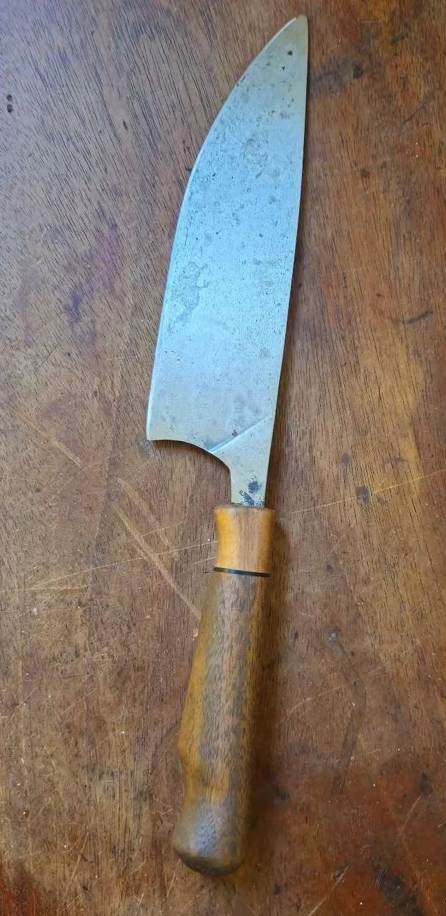 A large, rustic chef's knife with a wooden handle resting on a wooden surface.