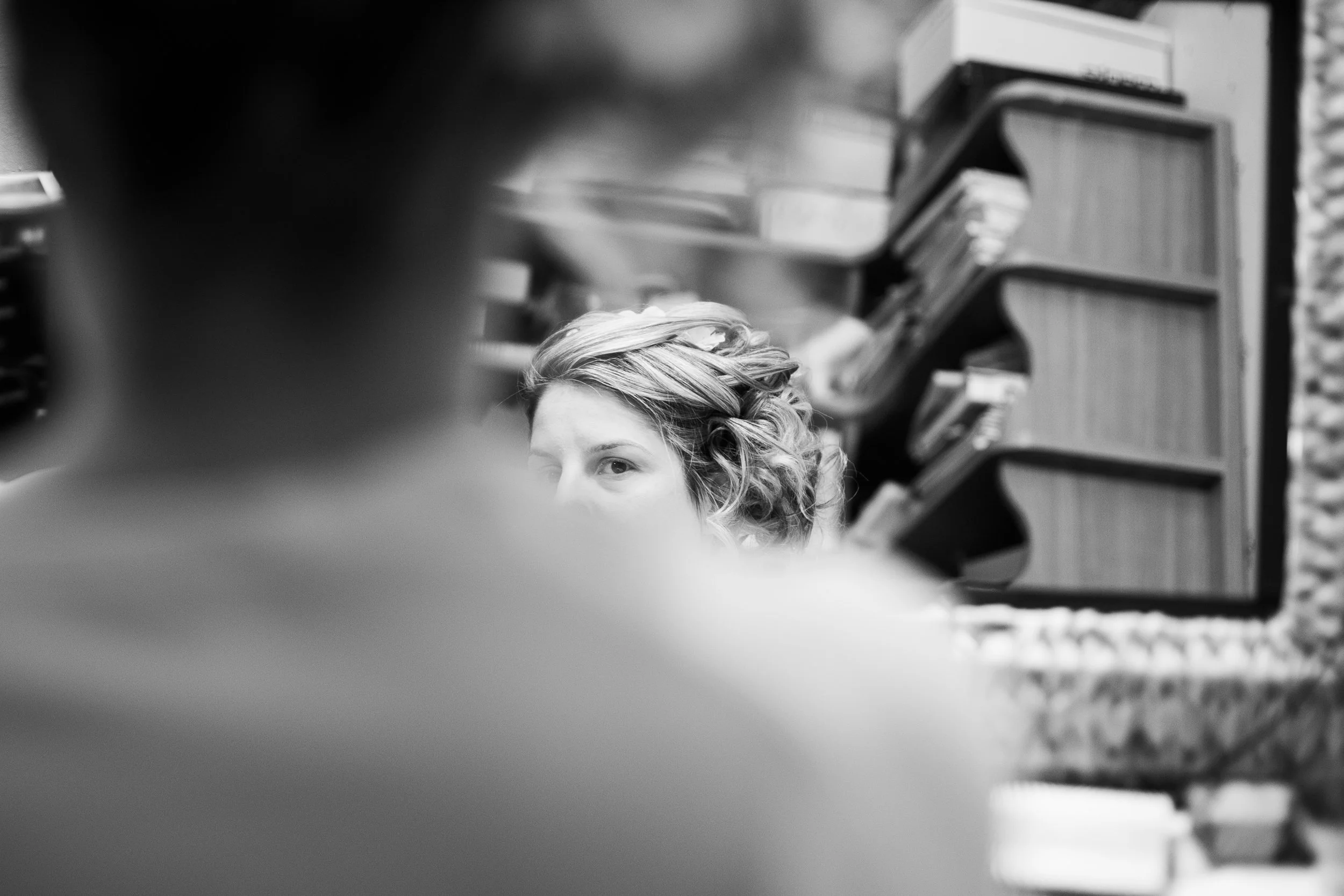 Une femme avec des cheveux bouclés, qui regarde par-dessus une étagère remplie de livres, dans un environnement intérieur.