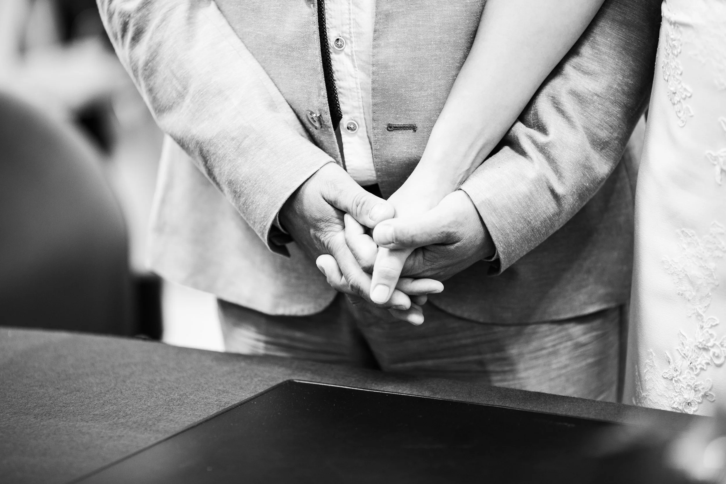 Une personne en costume lors d'une cérémonie, la main posée sur l'autre avant-bras, probablement en pleine écoute ou dans un discours, photo en noir et blanc.