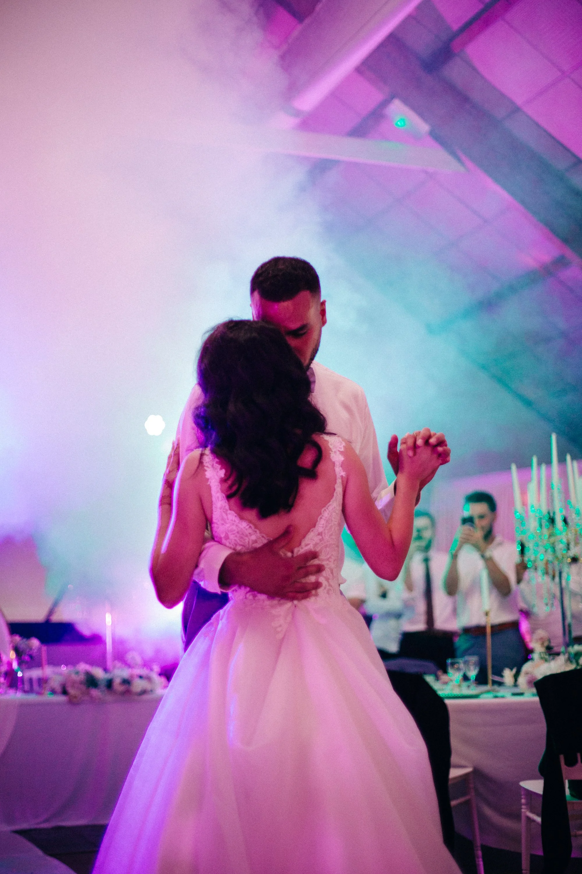 Un couple en robe de mariée danse lors d'une réception de mariage, avec des invités en arrière-plan