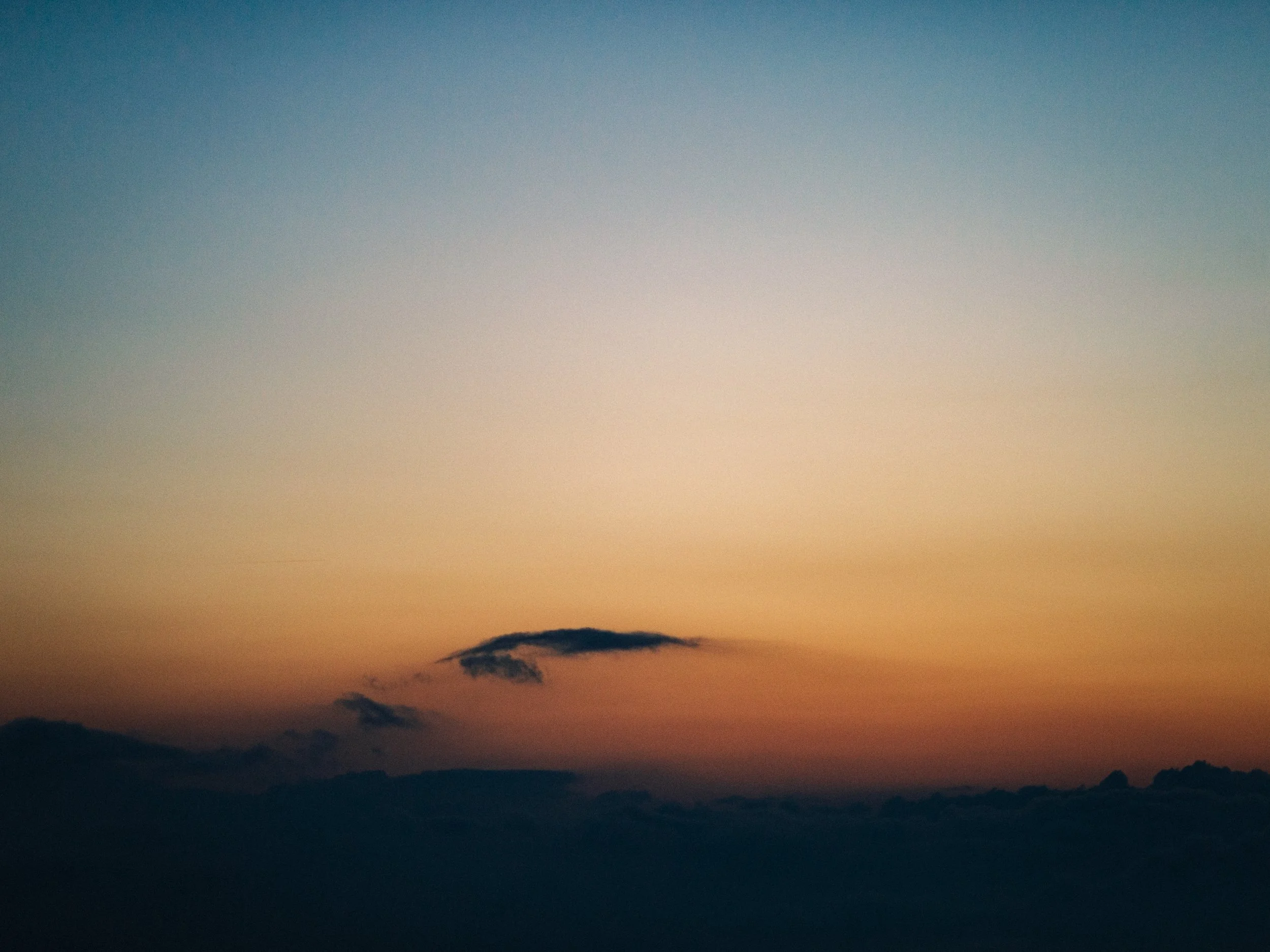 Coucher de soleil avec nuages au-dessus des montagnes, ciel aux teintes pastel, horizon lumineux.