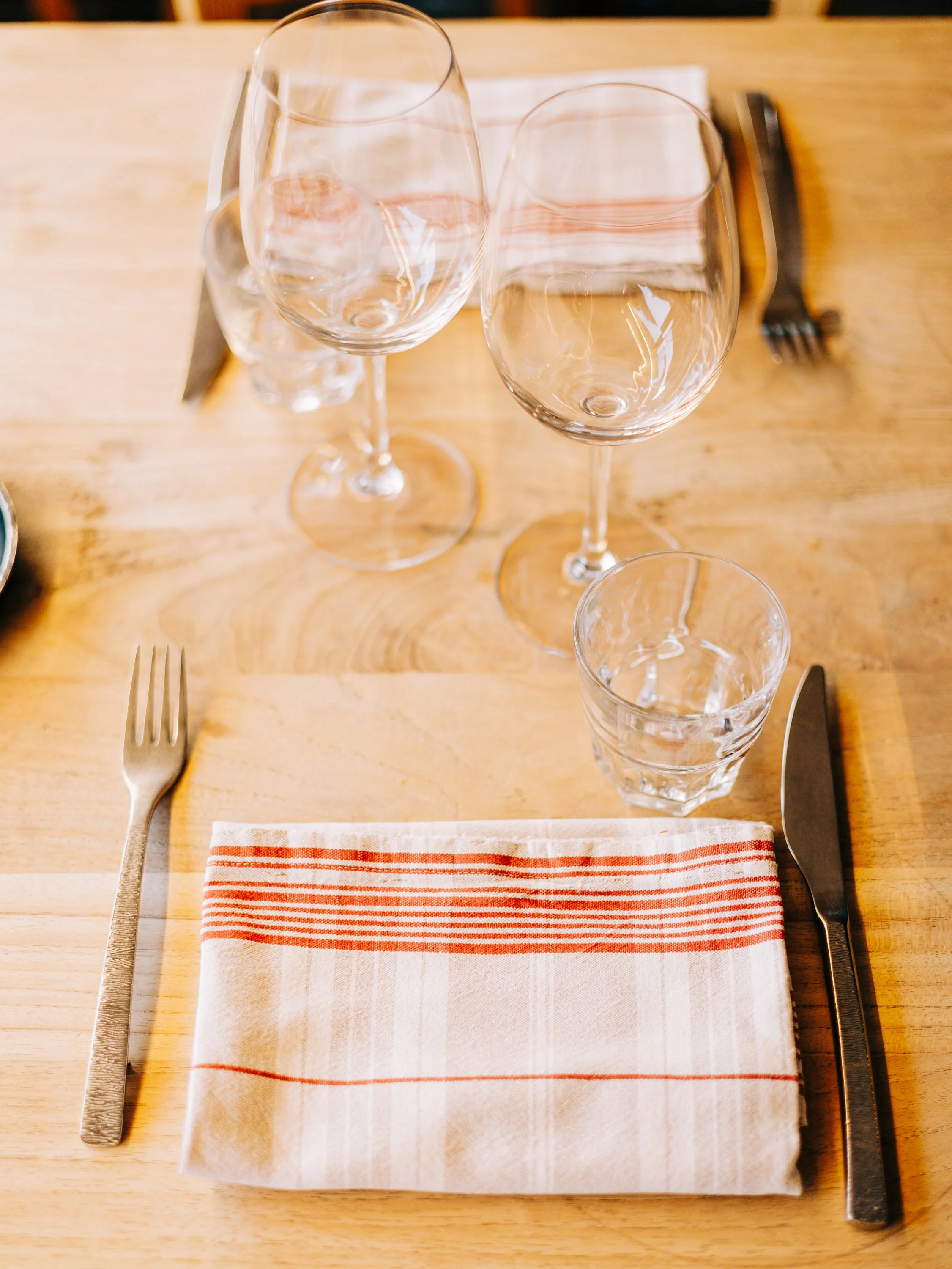 Vue d'une table avec deux verres à vin vides, une assiette, des couverts en métal, une serviette rayée rouge et blanche, et une nappe en tissu.