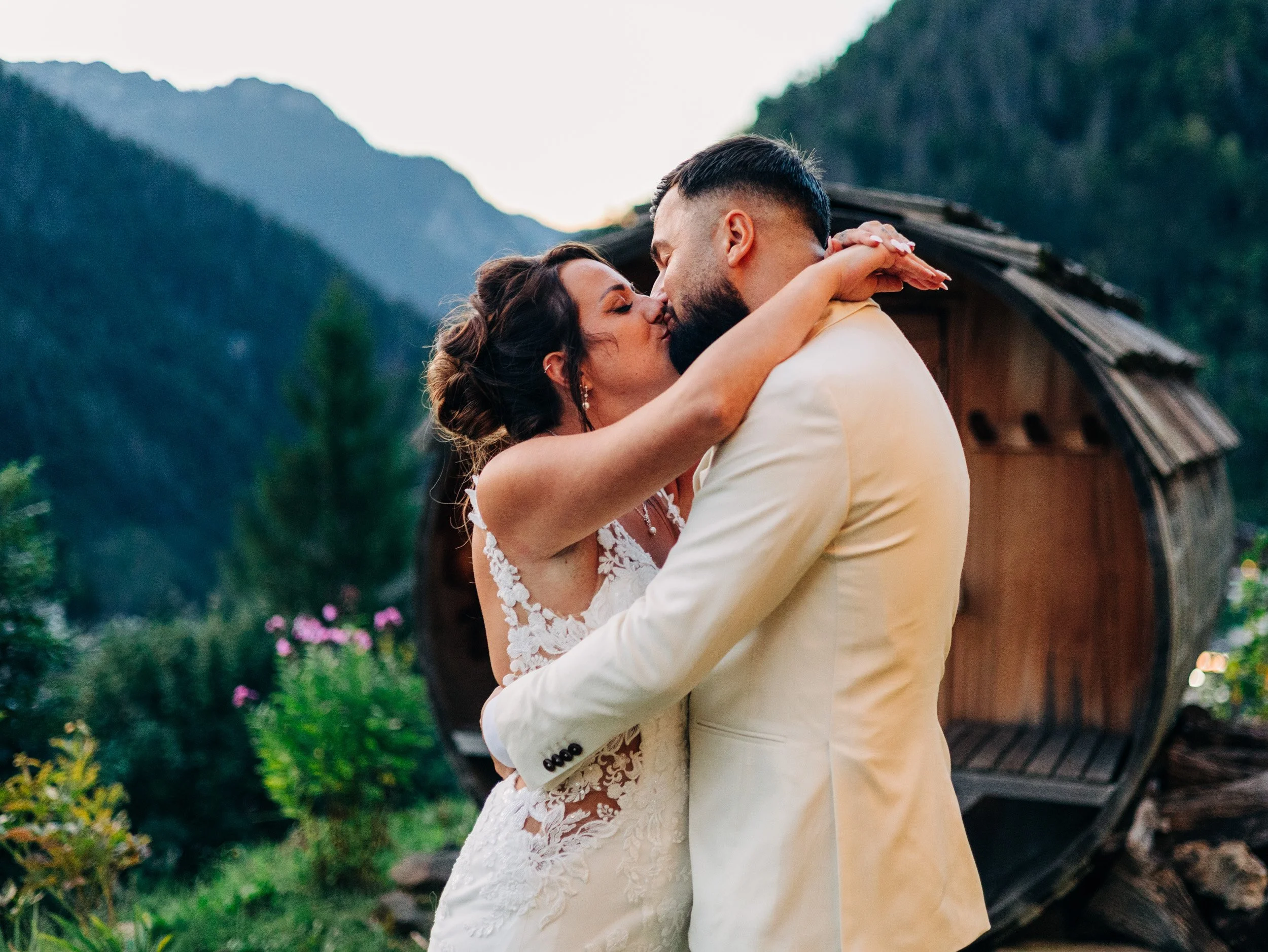 Un couple en tenue de mariage s'embrassant dans un cadre naturel avec des montagnes en arrière-plan.