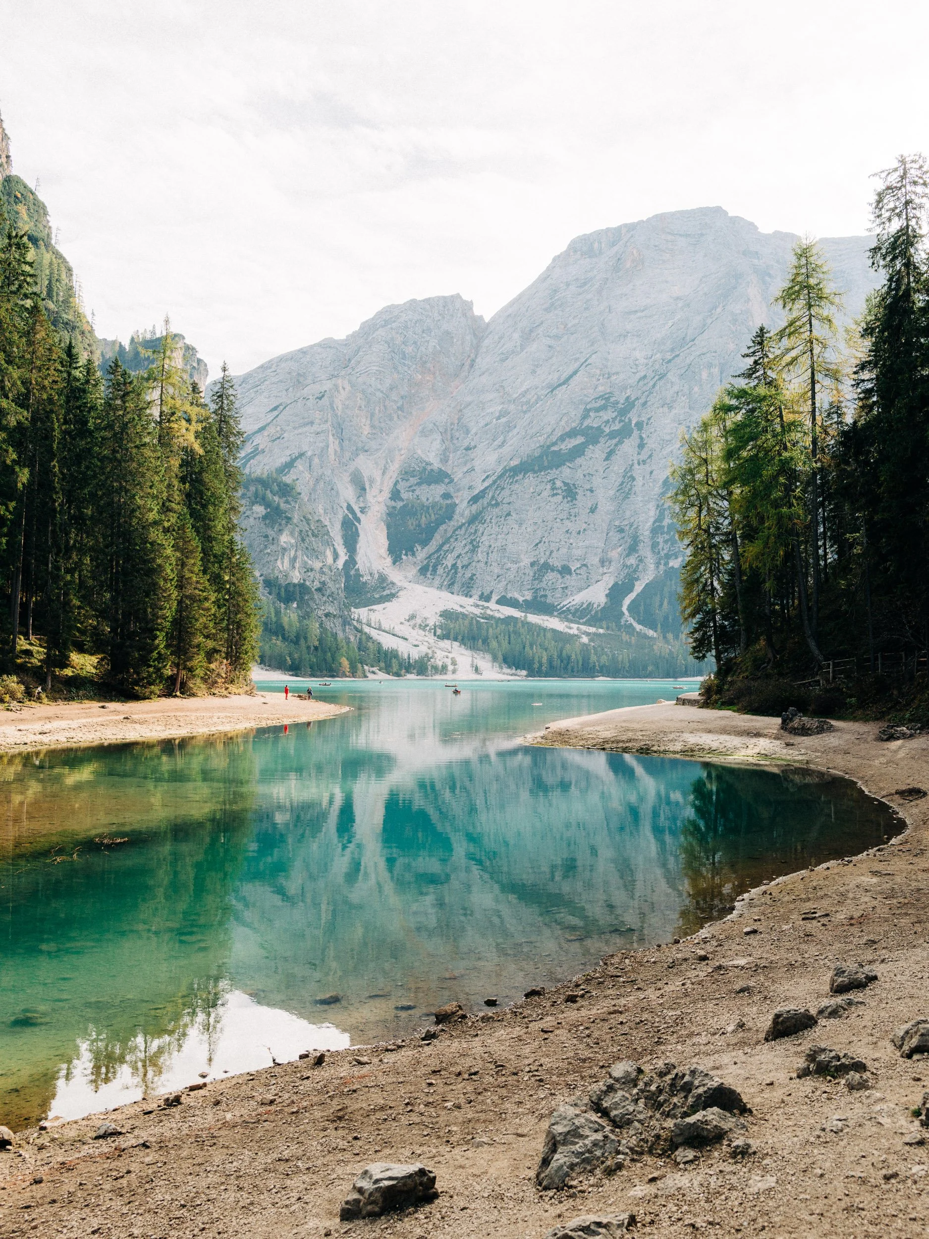 Lac turquoise entouré de montagnes rocheuses et de forêts de conifères, avec des personnes au bord de l'eau