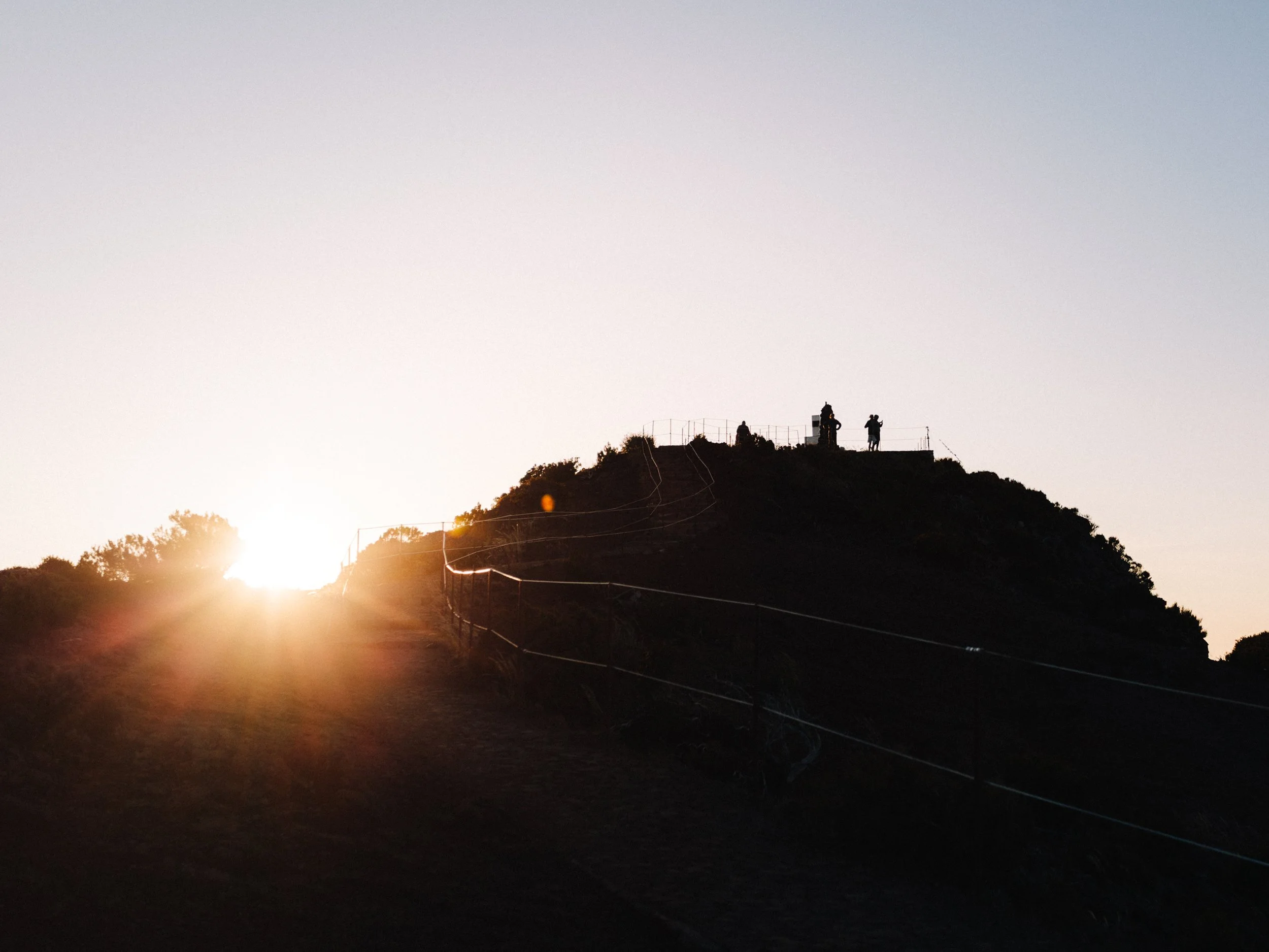 Silhouettes de personnes sur une colline au coucher du soleil avec un ciel clair.
