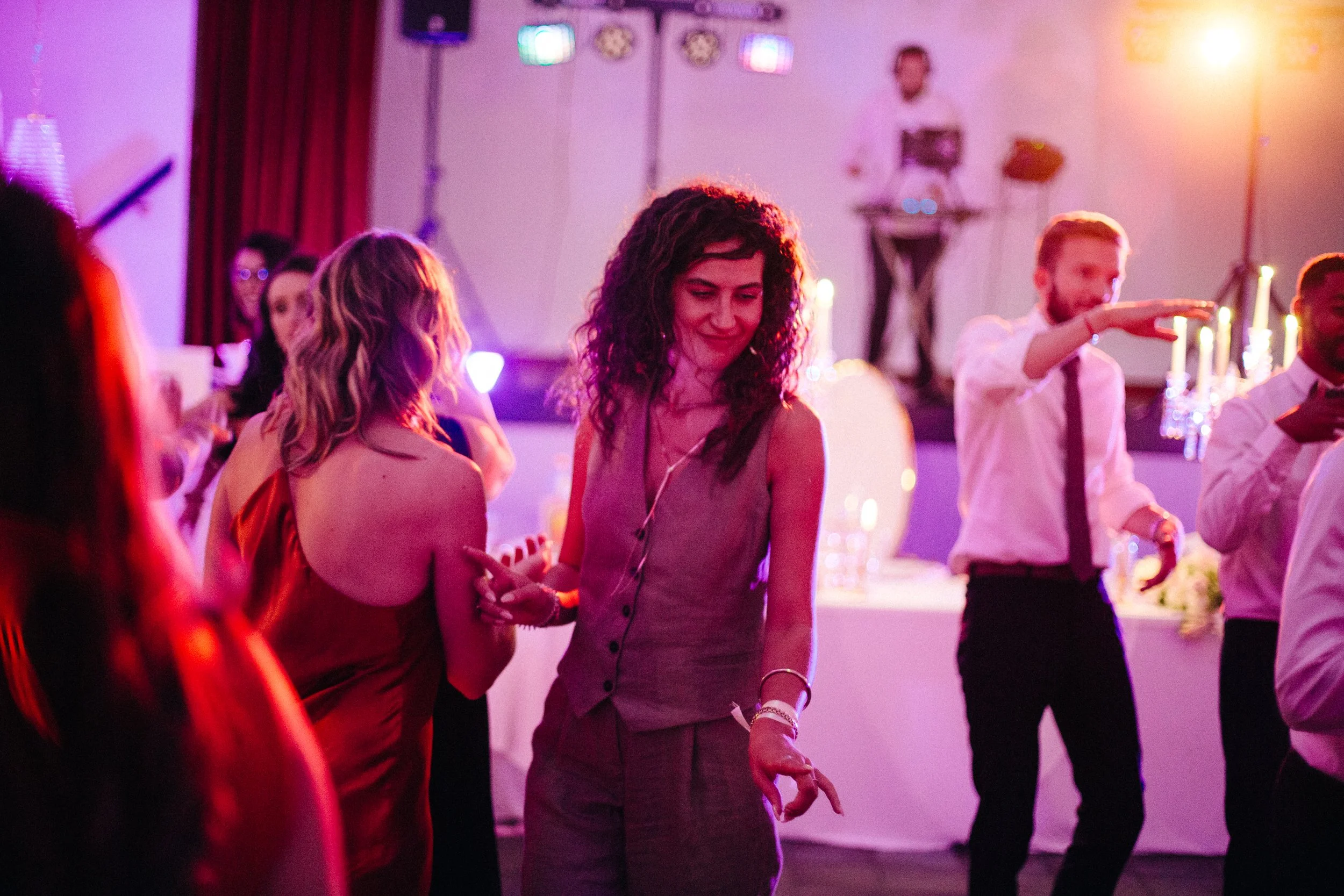 Des personnes dansant lors d'une soirée avec une ambiance colorée et lumière tamisée, un DJ en arrière-plan.