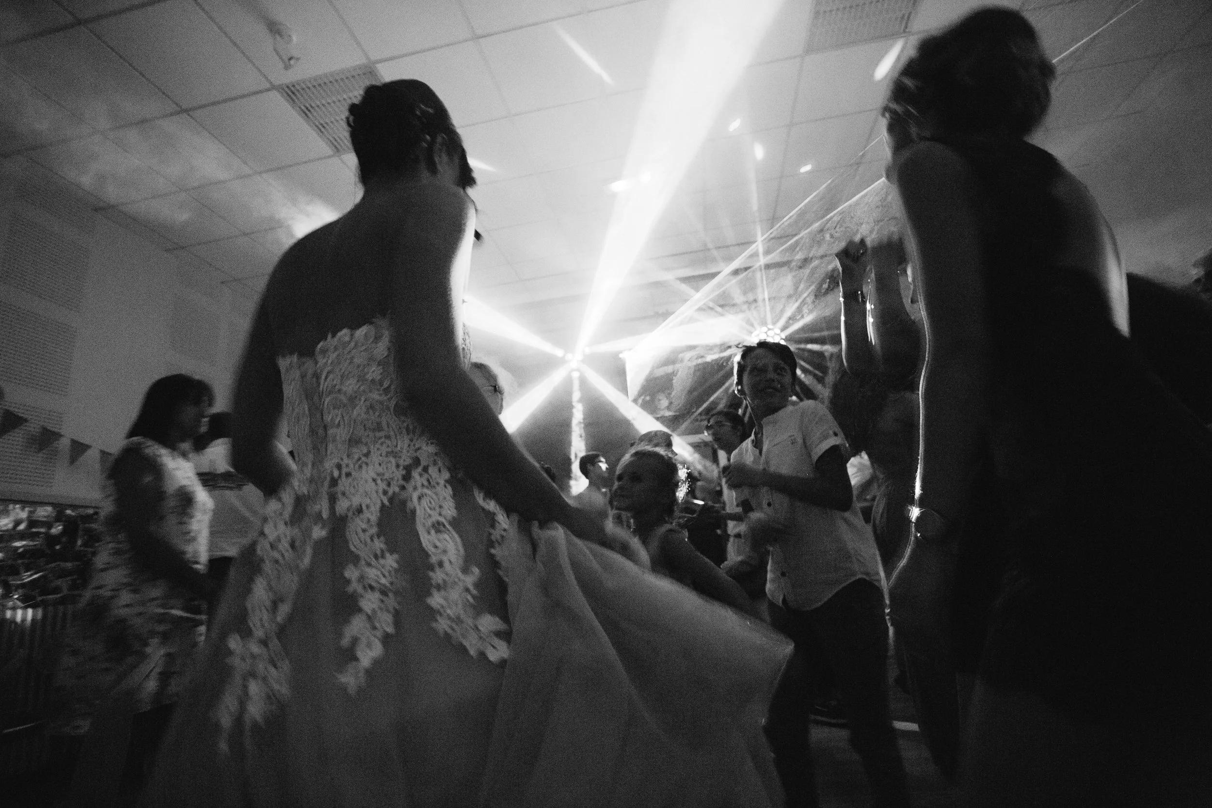 Des personnes dansant lors d'une fête ou d'un événement, avec des lumières laser en arrière-plan, en noir et blanc.
