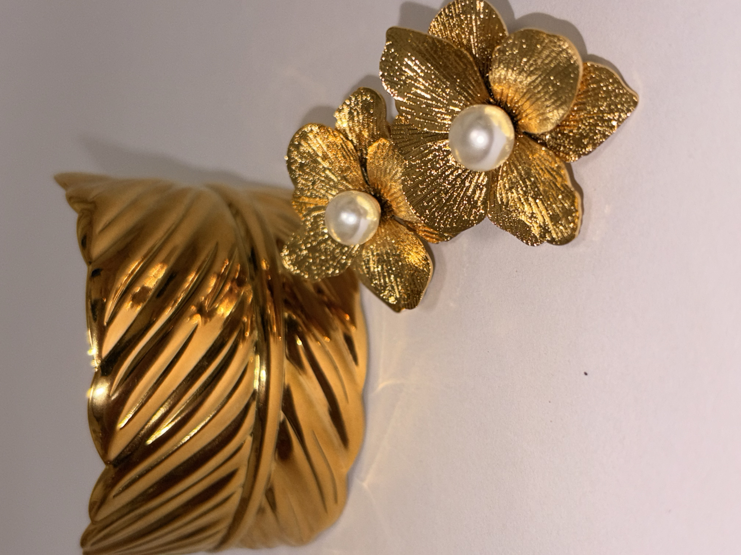 Pendientes dorados con forma de flor y perla en el centro, decorada con una pulsera con forma de hojas.