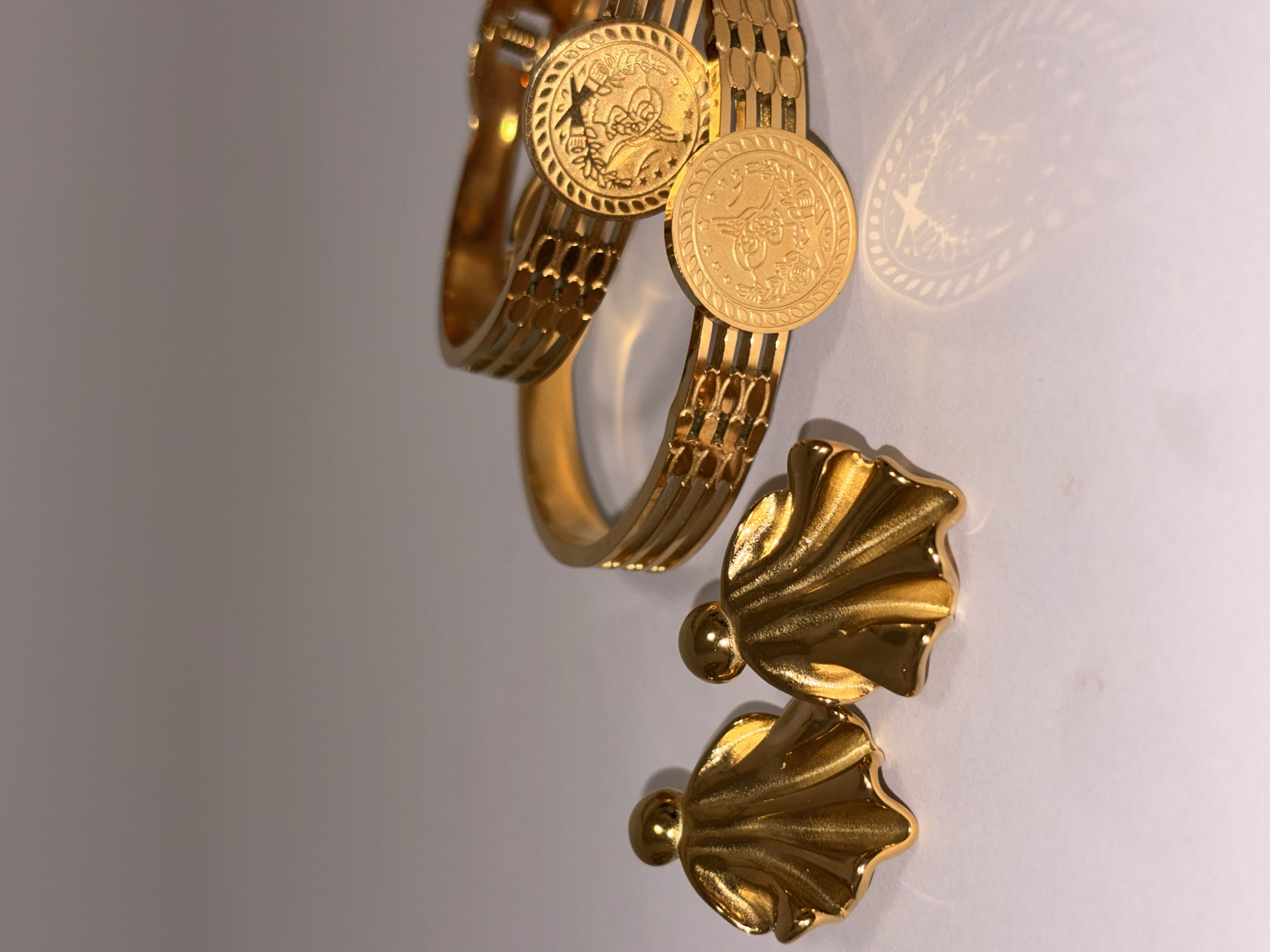 Pulsera dorada con monedas y unos pendientes con forma de ángel.
