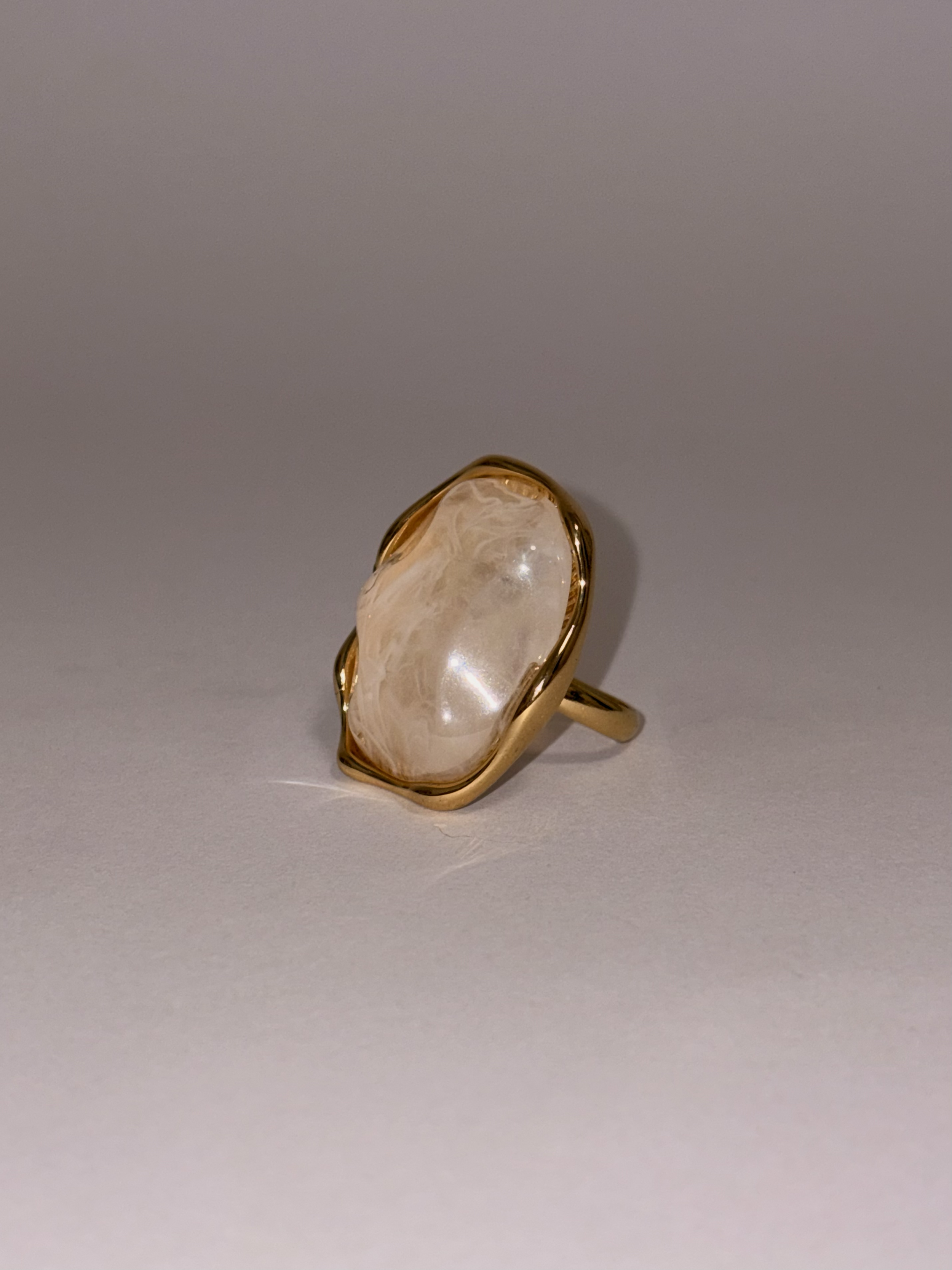 Anillo dorado con una piedra grande, irregular y traslúcida, en el centro.