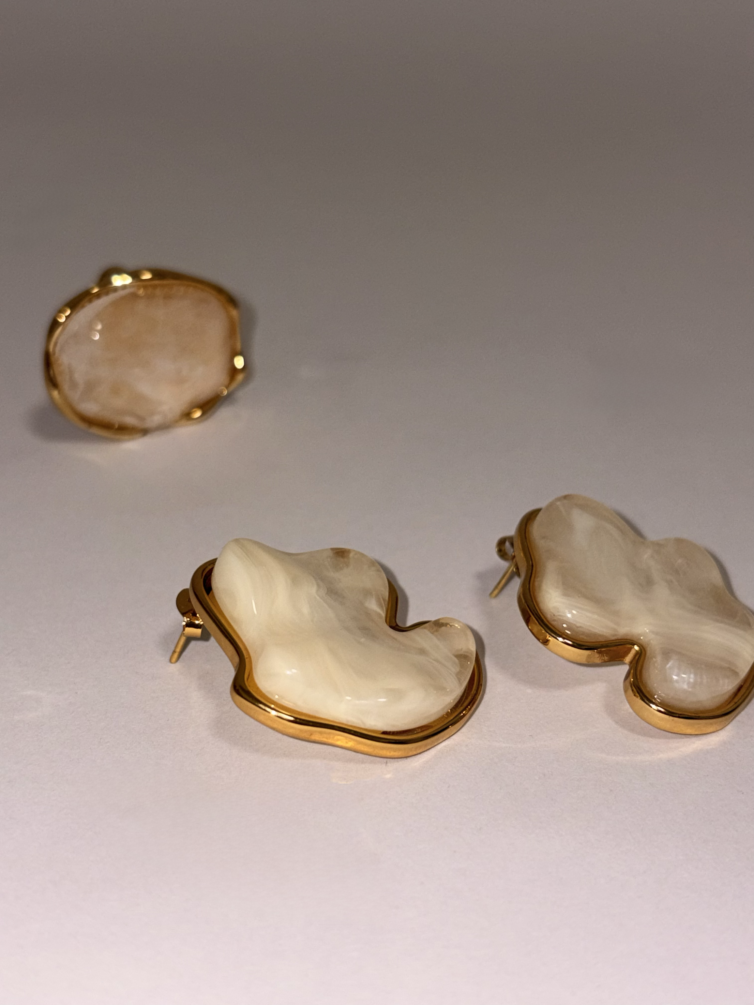 Pendientes de piedra en forma irregular con borde dorado, colocados sobre fondo claro.
