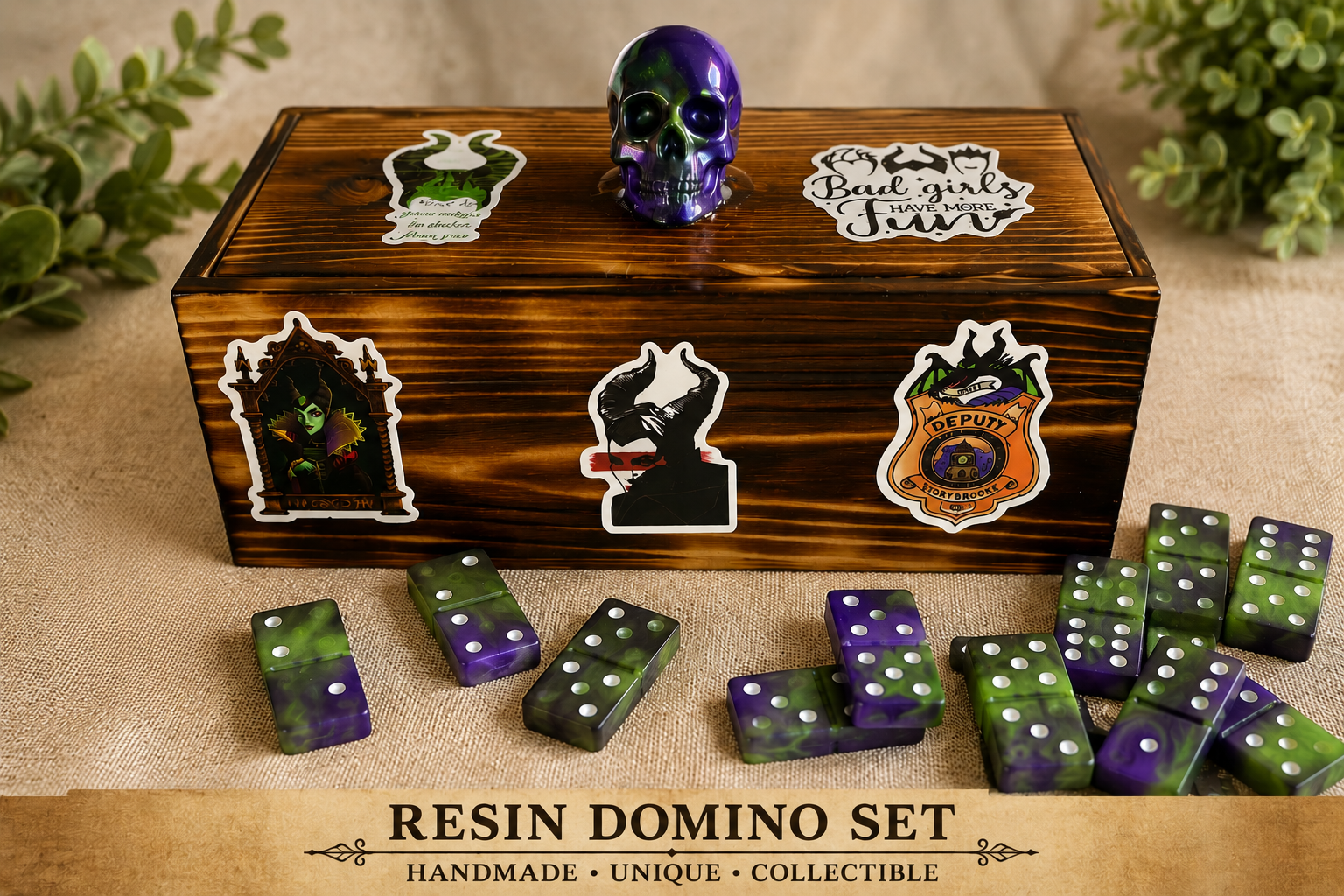 A resin domino set with purple and green dominoes, a decorative wooden box with Halloween-themed stickers, and a purple skull on top, with additional Halloween stickers on the box, placed on a beige fabric surface with greenery in the background.