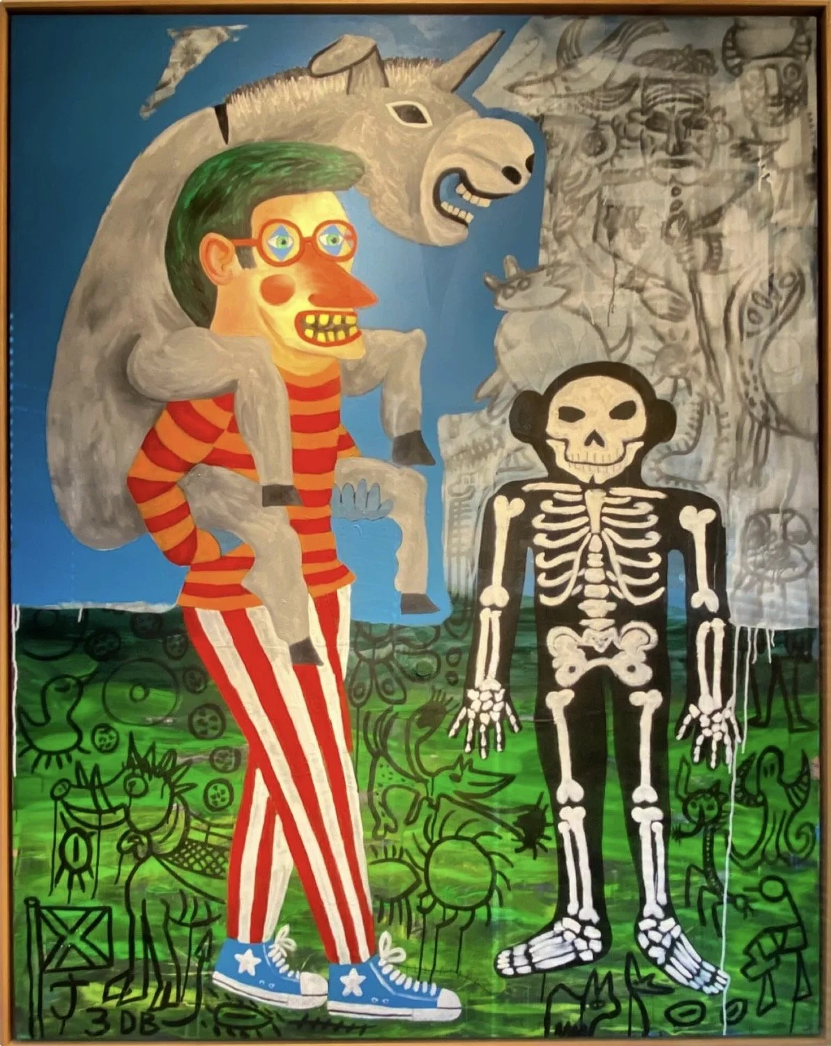 Une peinture colorée représentant un personnage avec un visage cartoon, des cheveux verts, portant une tenue rayée rouge et blanche, avec un cheval en arrière-plan, un squelette noir et blanc à côté, et divers dessins en noir en arrière-plan.