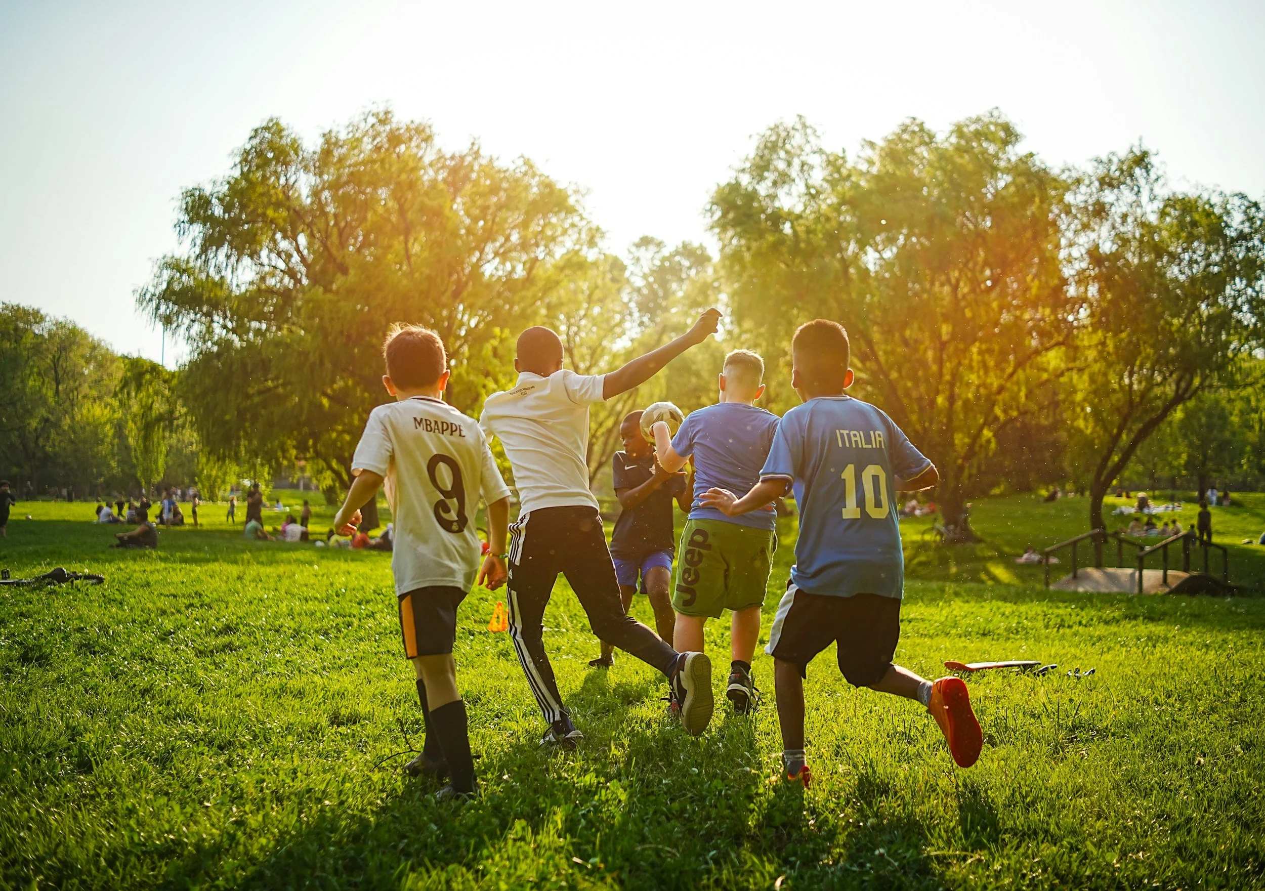 Children playing soccer outdoors in a park on a sunny day.