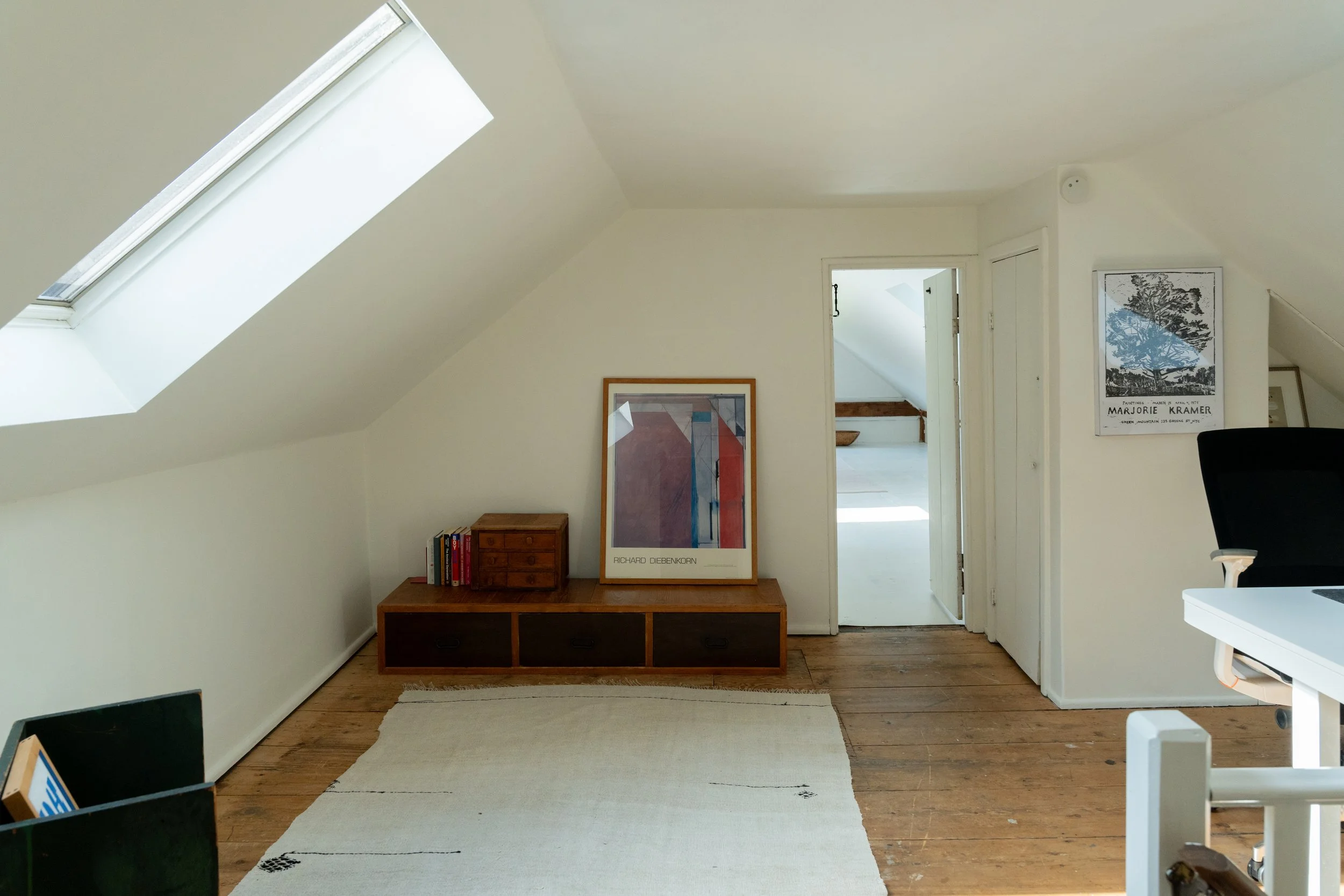 A cozy attic room with white sloped ceiling and a skylight window.