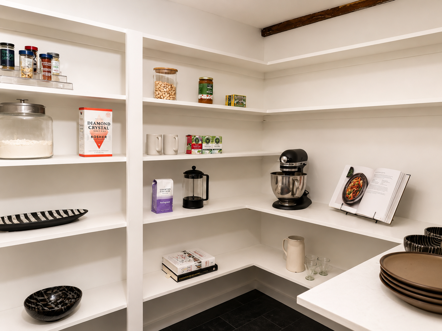 Empty kitchen pantry with white shelves, kitchen appliances, cookbooks, and dishes.