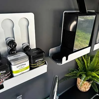 Lagerregal mit Gewürz- und Kaffeebehältern, Smartphone auf Ladestation, Pflanze in Dekokorb