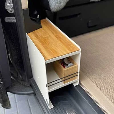 Ein kleiner, weißer Nachttisch mit Holzplatte, der an der Seite eines Autos steht und eine kleine Schublade enthält.